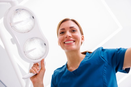 Female dentist adjusting light above dental chair